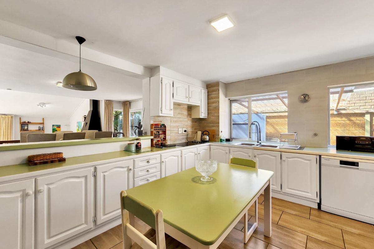 A functional kitchen featuring white cabinetry, tiled splashbacks, a ceramic hob, and an integrated dishwasher, with an open-plan layout connecting to the living area.