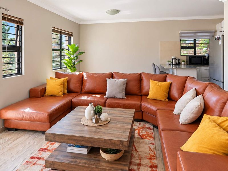 Spacious open-plan living area featuring tiled floors, large windows with security bars, and a seamless transition to the kitchen and staircase.