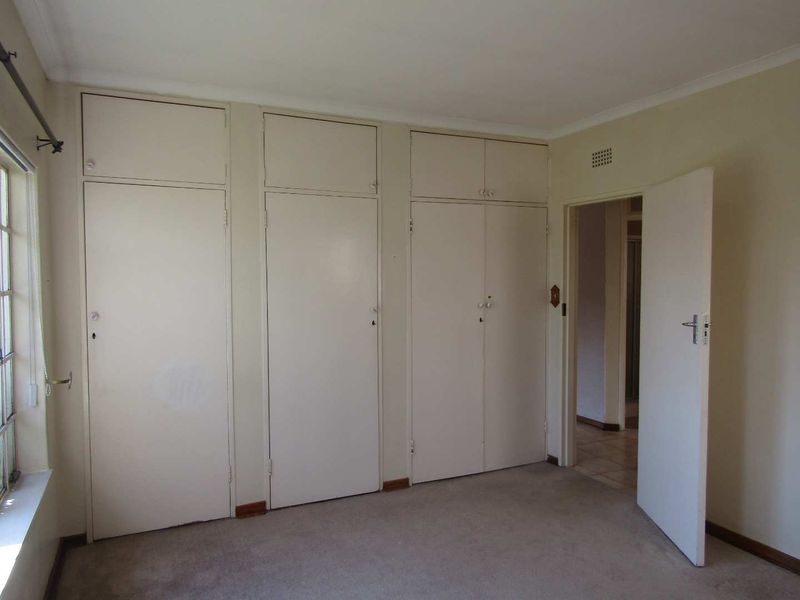 A vacant bedroom featuring built-in cupboards, neutral wall finishes, and carpeted flooring, offering a blank canvas for potential updates.