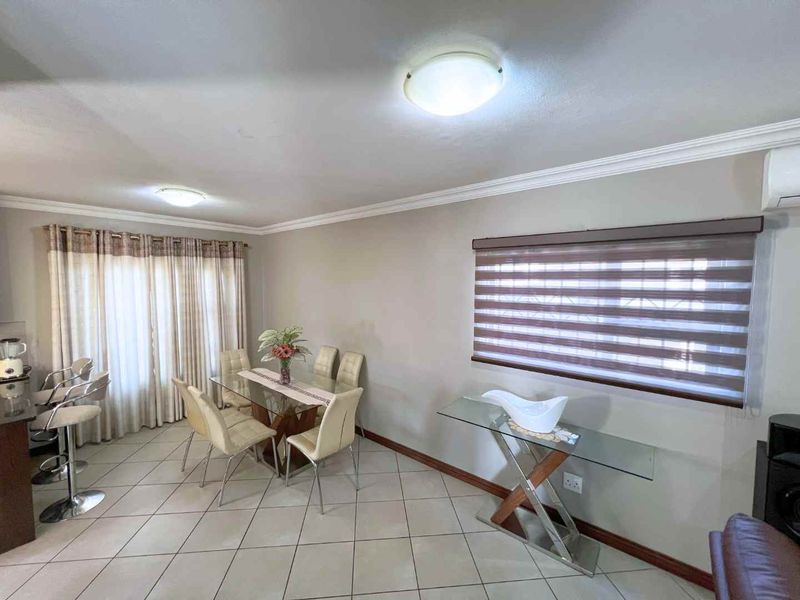 A well-maintained dining area featuring neutral tiled flooring, modern window treatments, and a split-system air conditioning unit.