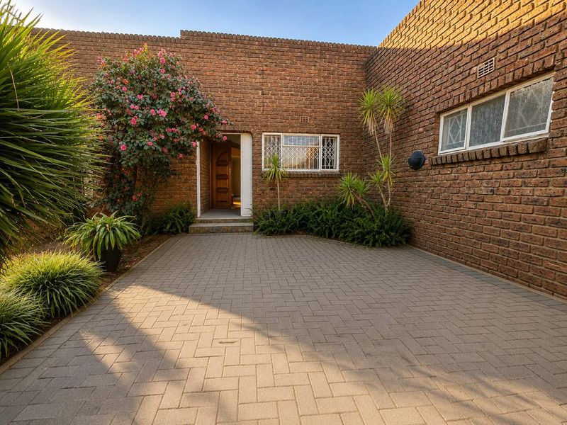 A well-maintained front entrance featuring a classic brick facade, paved driveway, and secure window detailing, providing a welcoming and solid street appeal.