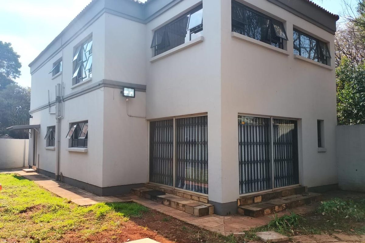 A double-story cluster home exterior featuring tiled patio areas, security gates, and aluminum window frames set within a private garden space.