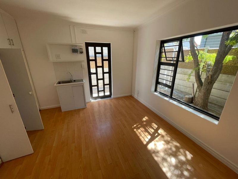 A compact, empty kitchen area featuring laminate flooring, built-in cabinetry with a sink, and a large window providing natural light.