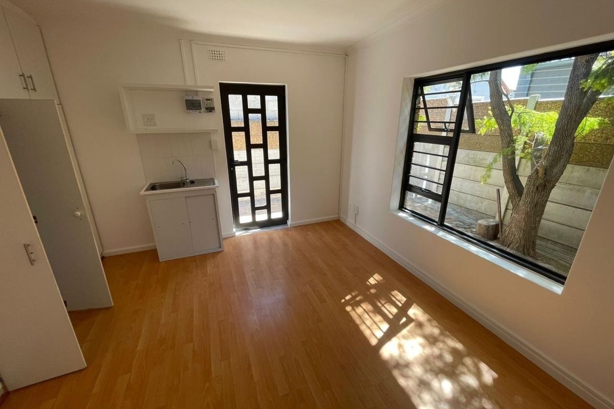 A compact, empty kitchen area featuring laminate flooring, built-in cabinetry with a sink, and a large window providing natural light.