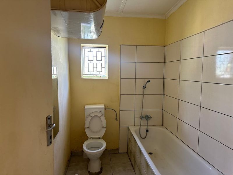 A functional bathroom featuring a bathtub with handheld shower attachment, toilet, and tiled wall finishes, requiring cosmetic updates to improve its overall condition.