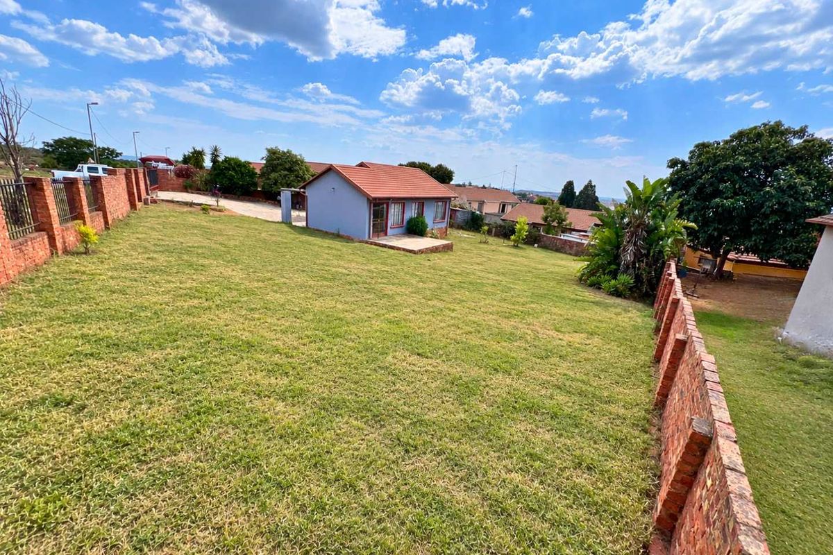 A spacious rear garden featuring a large lawn, brick boundary walls, and a detached dwelling with a tiled roof and small concrete patio.