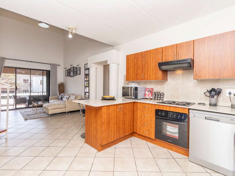 Open-plan living area featuring a functional kitchen with wood-finish cabinetry, integrated appliances, and tiled flooring, flowing seamlessly into a bright lounge with balcony access.