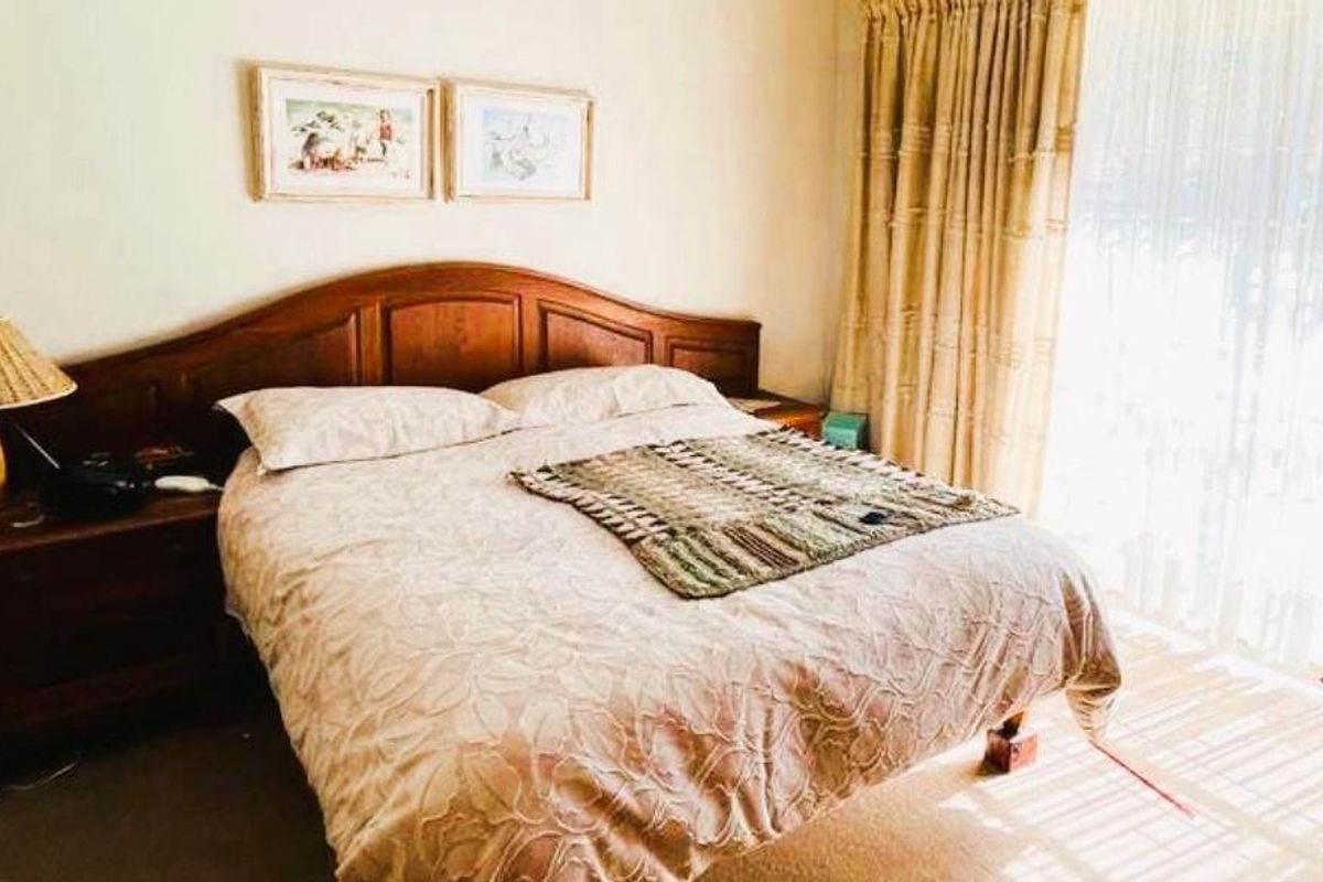 A bedroom featuring a built-in wooden headboard and large sliding glass doors with curtains, providing natural light and access to the exterior.