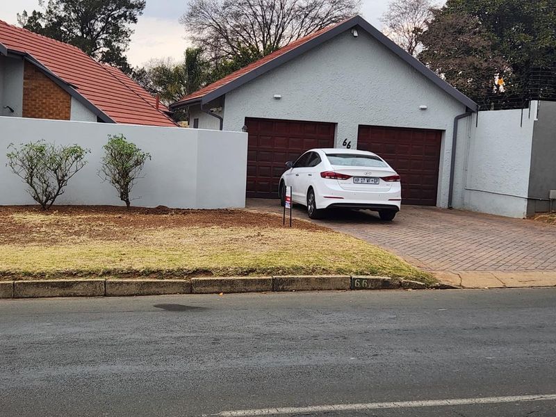 Front view of the property featuring a double garage, paved driveway, and secure boundary wall with electric fencing.