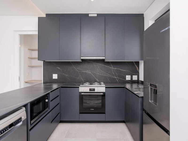 Modern kitchen featuring dark grey cabinetry, stone countertops, a matching backsplash, and high-quality built-in appliances including an oven, cooktop, and dishwasher.
