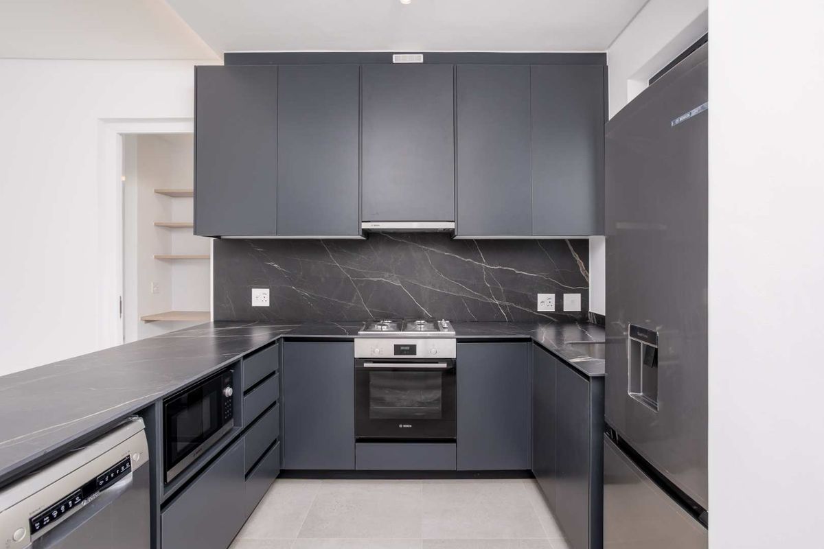 Modern kitchen featuring dark grey cabinetry, stone countertops, a matching backsplash, and high-quality built-in appliances including an oven, cooktop, and dishwasher.