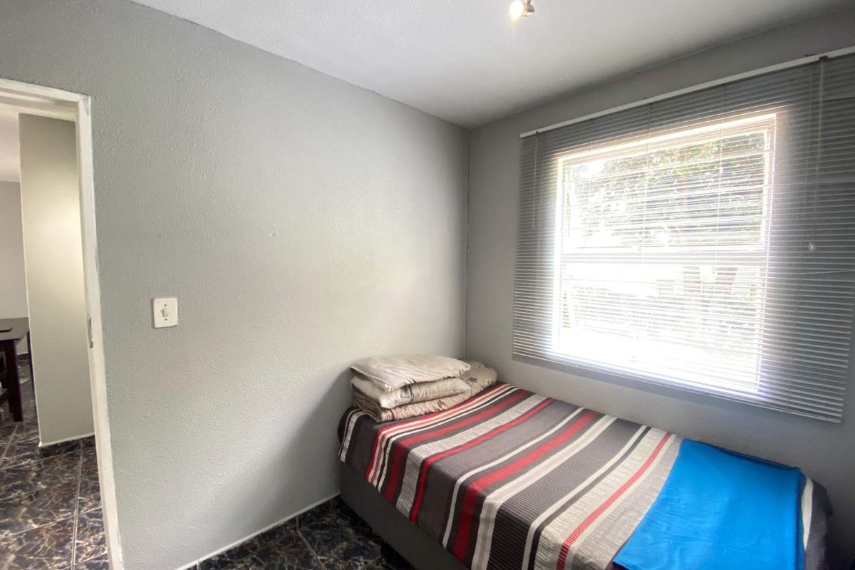 A compact bedroom featuring tiled flooring, a window with fitted blinds, and neutral grey wall finishes.