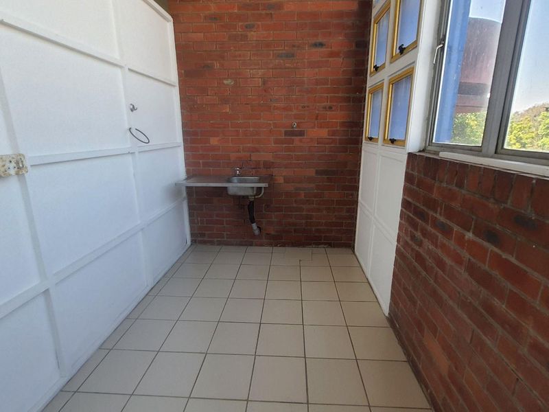 A functional utility or laundry space featuring exposed brick walls, tiled flooring, and a wall-mounted sink with natural light from casement windows.
