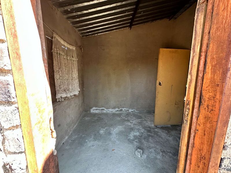 A basic, unfinished room featuring concrete flooring, plastered walls, and a corrugated metal roof, requiring significant renovation and cosmetic updates.