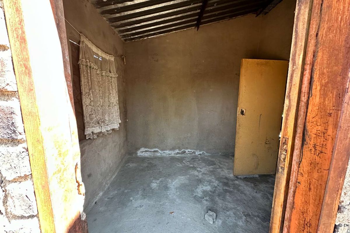 A basic, unfinished room featuring concrete flooring, plastered walls, and a corrugated metal roof, requiring significant renovation and cosmetic updates.