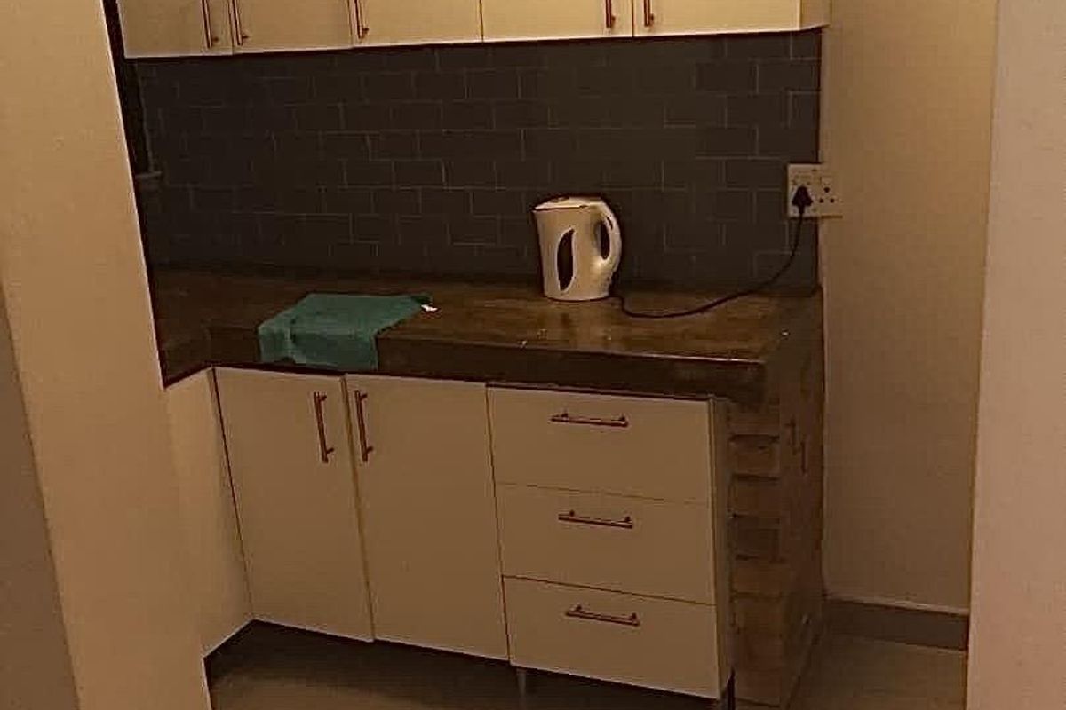A compact kitchen area featuring white cabinetry, a dark tiled backsplash, and stone countertops, currently in need of finishing touches to the base structure.