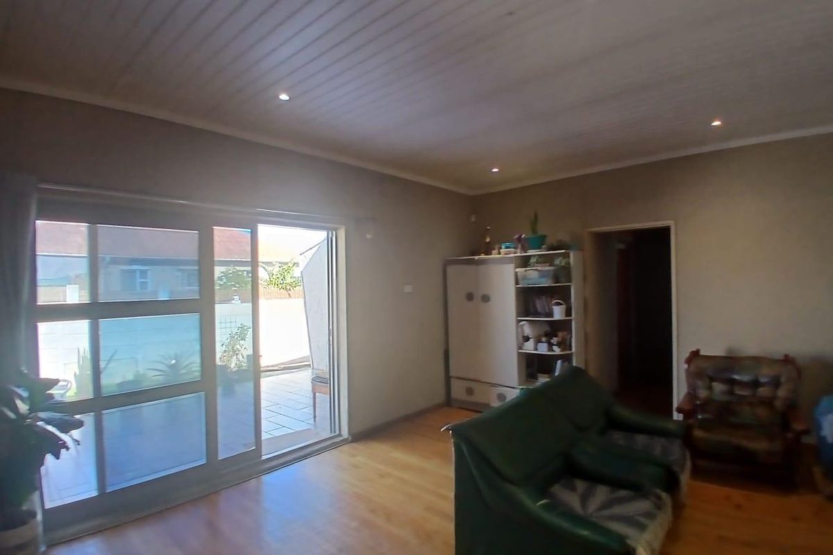 A living room featuring timber-look flooring, recessed downlighting, and large sliding glass doors providing direct access to an outdoor patio area.
