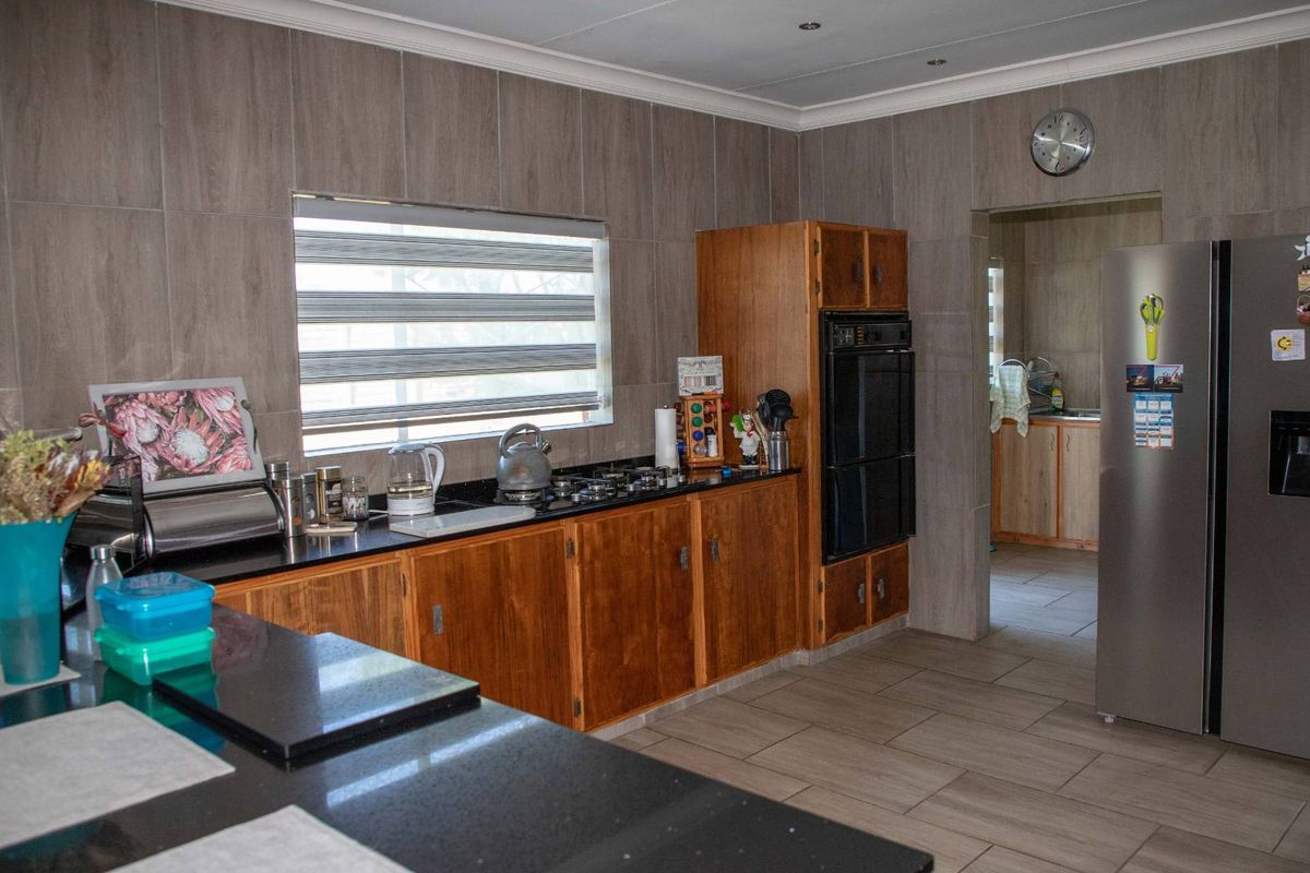 A functional kitchen featuring wooden cabinetry, black granite countertops, a built-in double oven, and tiled wall finishes, with an adjacent scullery area.