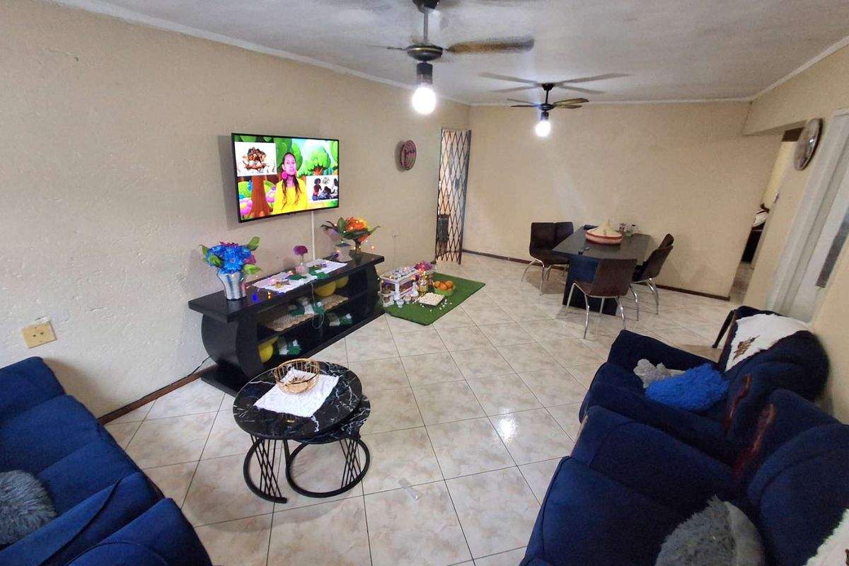 Open-plan living area featuring tiled flooring, dual ceiling fans, and a security gate, providing a functional space for relaxation and dining.