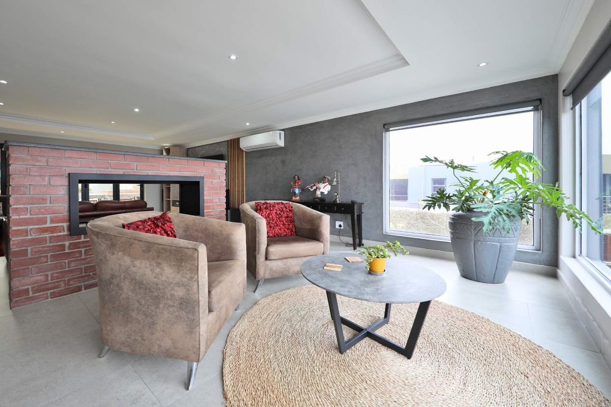 Modern living area featuring a distinctive exposed brick fireplace partition, recessed ceiling lighting, large windows, and neutral tiled flooring.