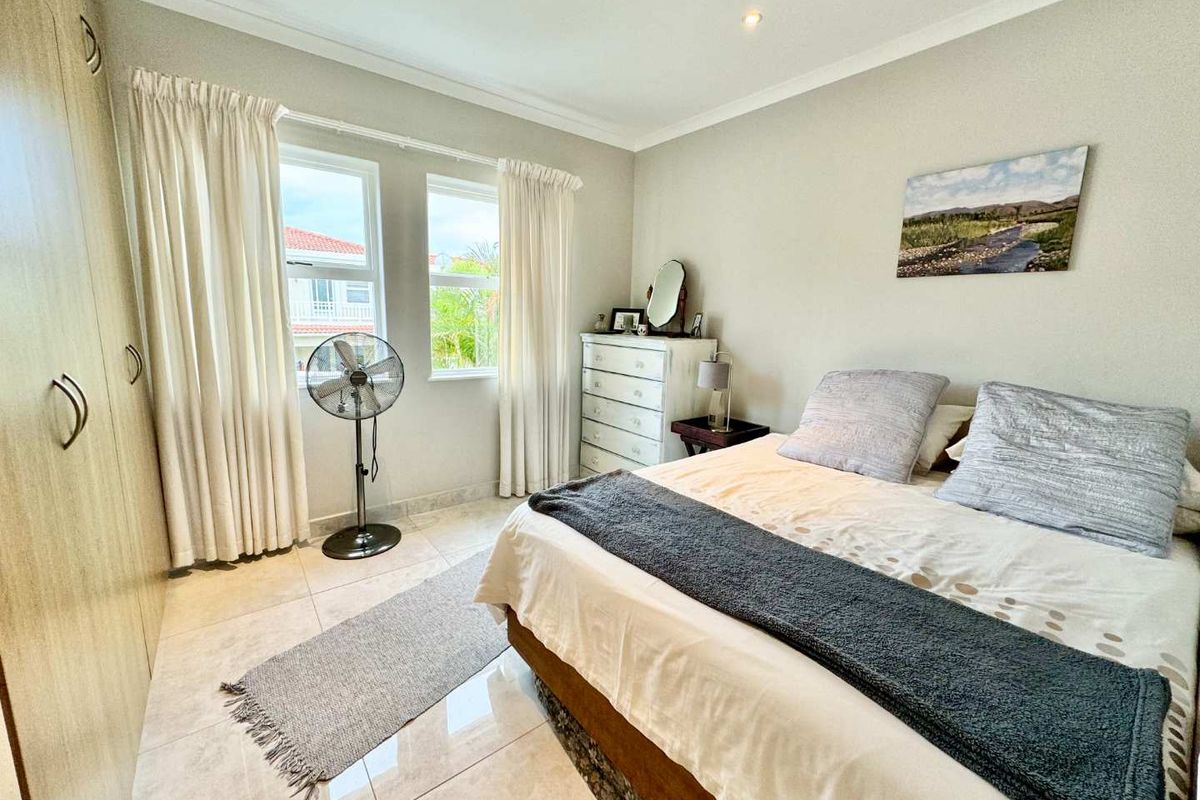 A well-maintained bedroom featuring neutral tiled flooring, built-in cupboards, and natural light through large windows with fitted curtain tracks.
