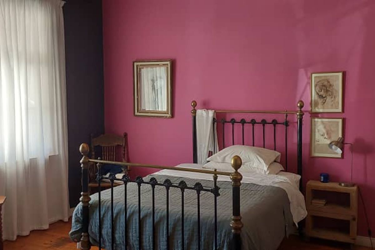 A bedroom featuring bold pink and dark blue accent walls, large windows with sheer curtains, and original wooden flooring.