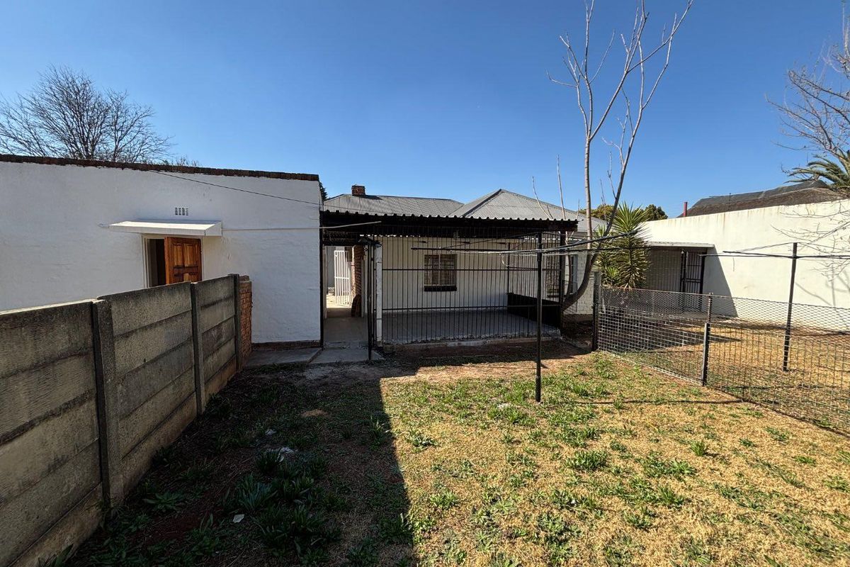 Rear exterior view of the property featuring a small garden, a covered patio area, and secure boundary walling.