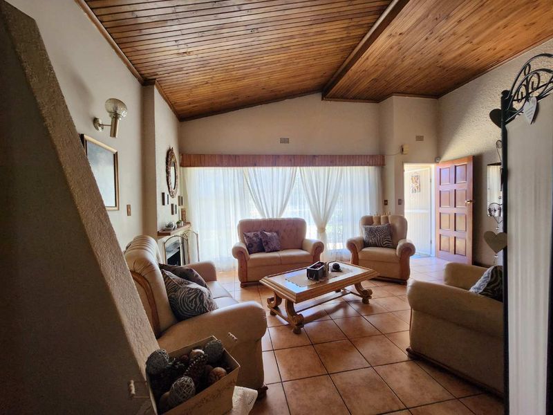 Spacious living room featuring a vaulted timber ceiling, tiled flooring, and a fireplace, offering a warm and inviting atmosphere with natural light.
