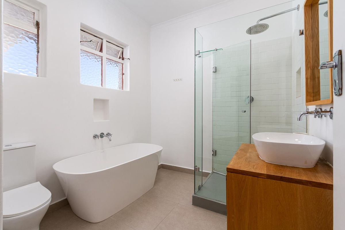 Modern bathroom featuring a freestanding bathtub, glass-enclosed shower with subway tiling, and a wooden vanity with a vessel sink.