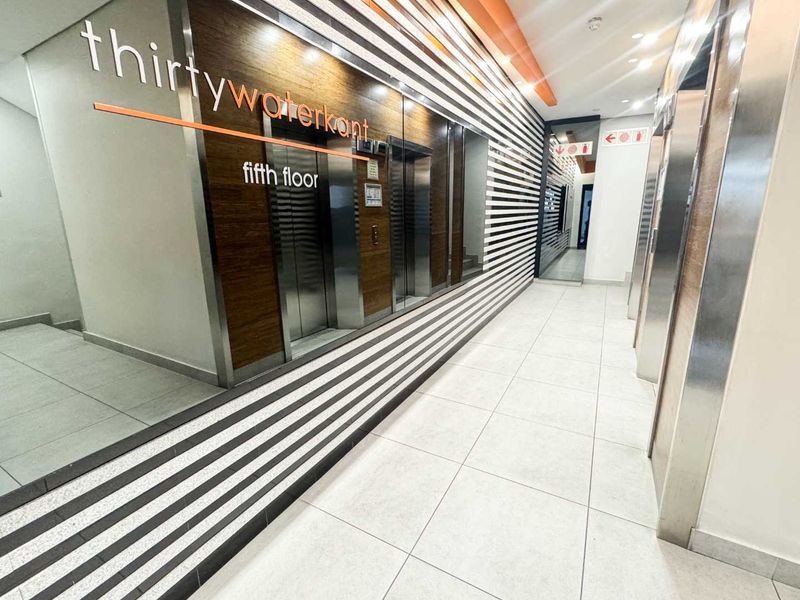 Modern office building elevator lobby featuring sleek tiled floors, decorative wall paneling, and stainless steel elevator doors on the fifth floor.
