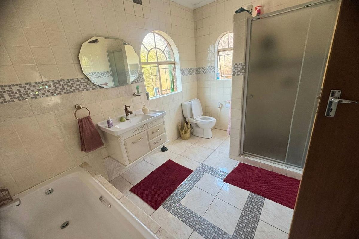 A functional bathroom featuring a built-in bathtub, a separate glass-enclosed shower, a vanity basin, and a toilet with arched windows.