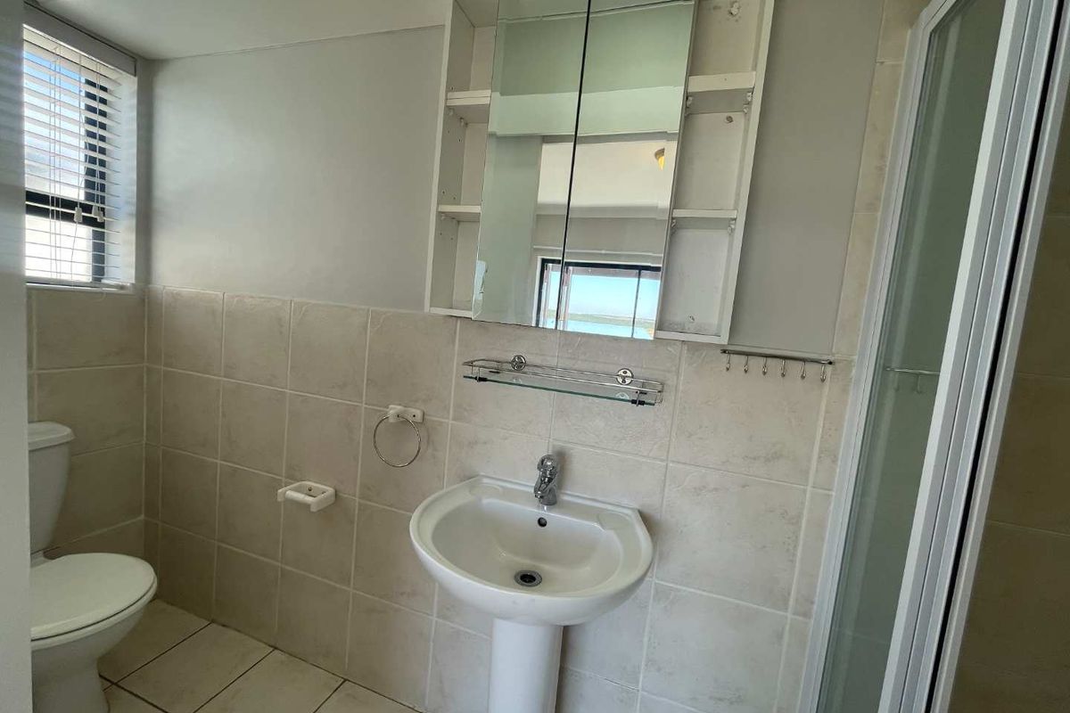 A functional bathroom featuring a pedestal basin, toilet, shower enclosure, and mirrored medicine cabinet with neutral wall and floor tiling.