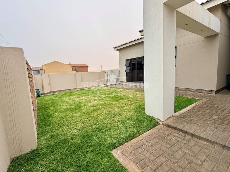 A well-maintained rear garden featuring a paved patio area, manicured lawn, and secure boundary walls, providing a private outdoor space.