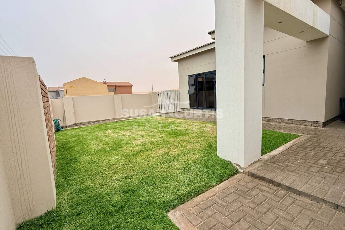 A well-maintained rear garden featuring a paved patio area, manicured lawn, and secure boundary walls, providing a private outdoor space.