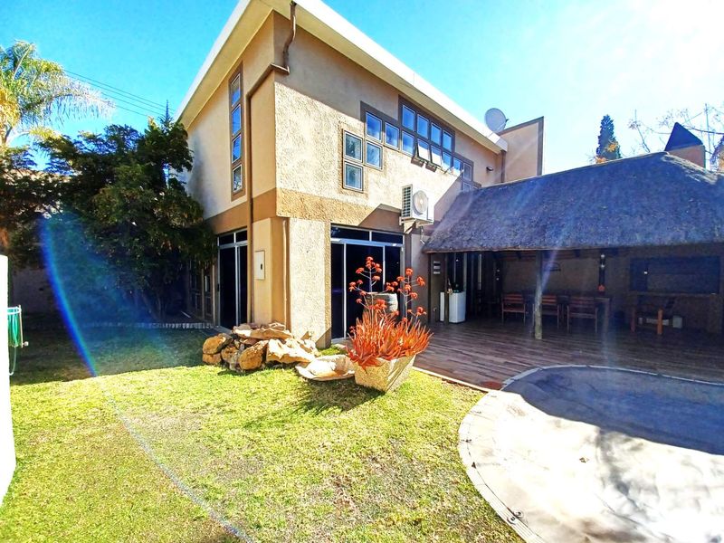 Rear view of the property featuring a thatched patio area, wooden decking, swimming pool, and sliding glass doors leading into the home.