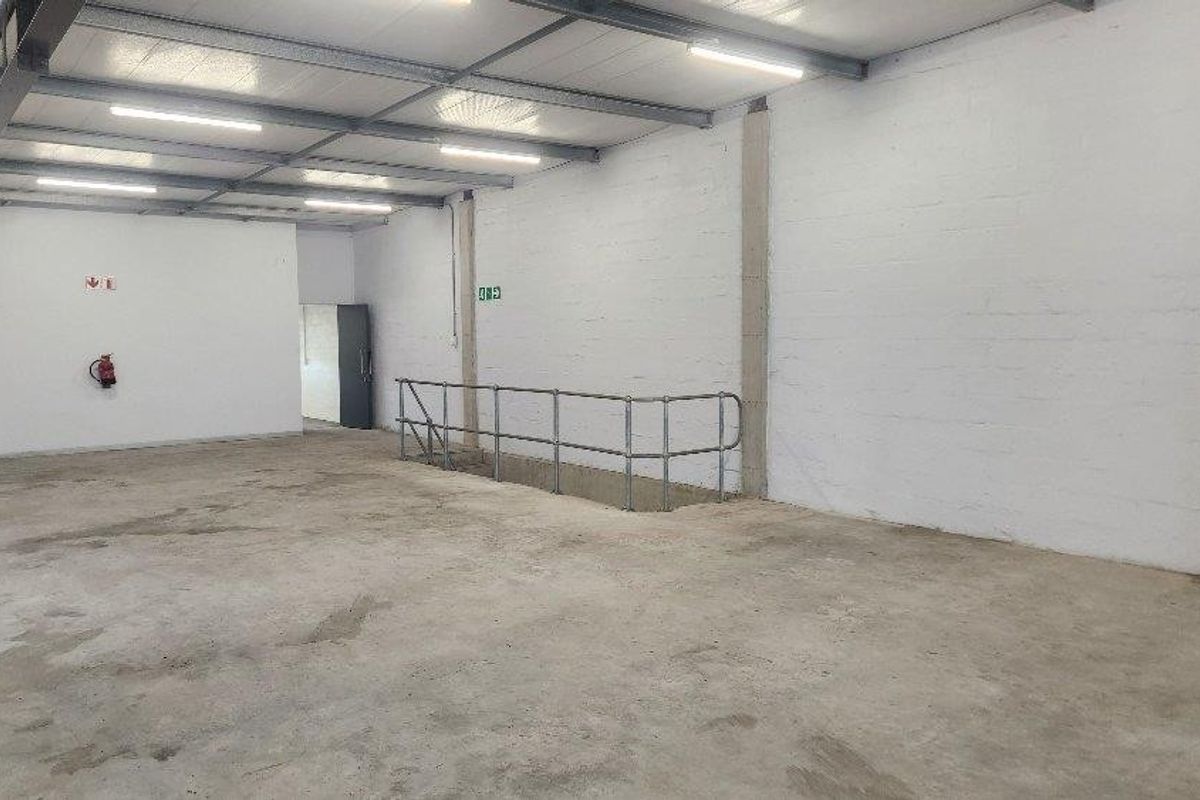 Spacious industrial utility area featuring exposed steel roof trusses, concrete flooring, and functional safety railings, suitable for storage or workshop use.
