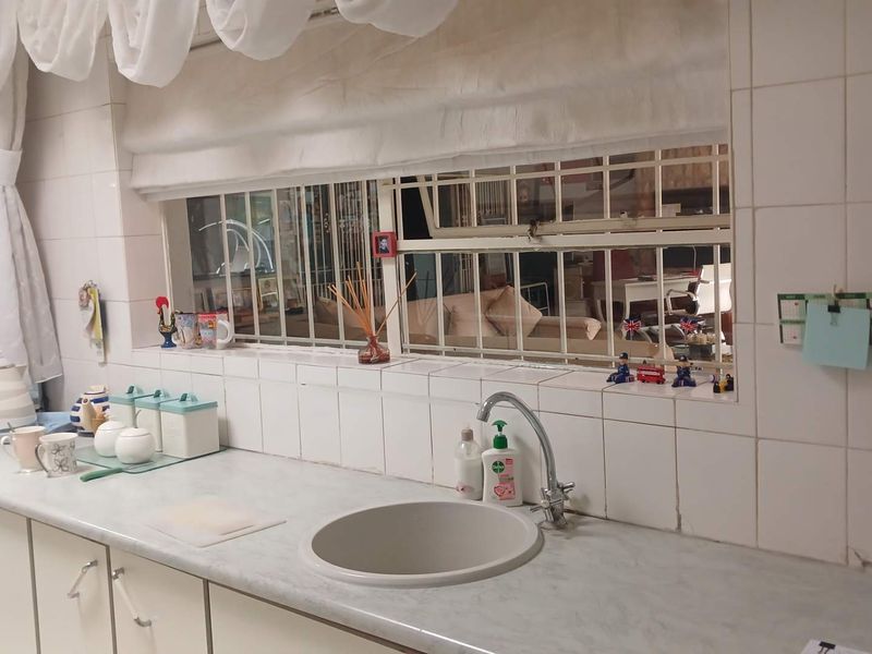 A functional kitchen area featuring a laminate countertop, built-in sink with mixer tap, and tiled splashback with security-barred windows.