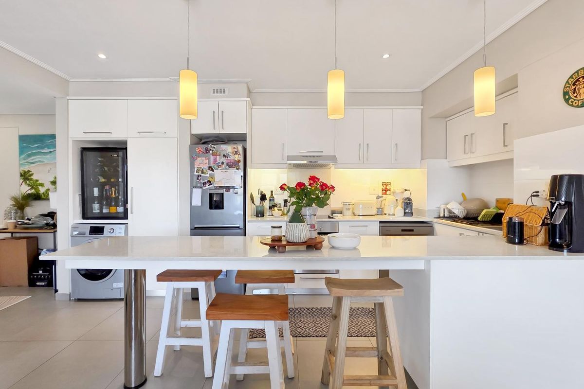 Modern kitchen featuring white cabinetry, a spacious quartz-topped island with breakfast seating, integrated appliances, and contemporary pendant lighting.