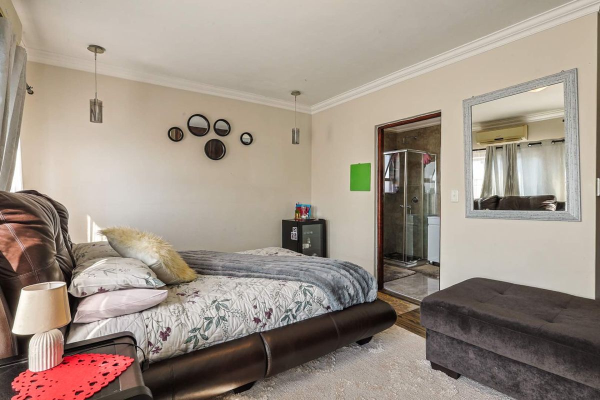 A well-maintained bedroom featuring an en-suite bathroom with a glass shower enclosure, neutral wall tones, and decorative pendant lighting.