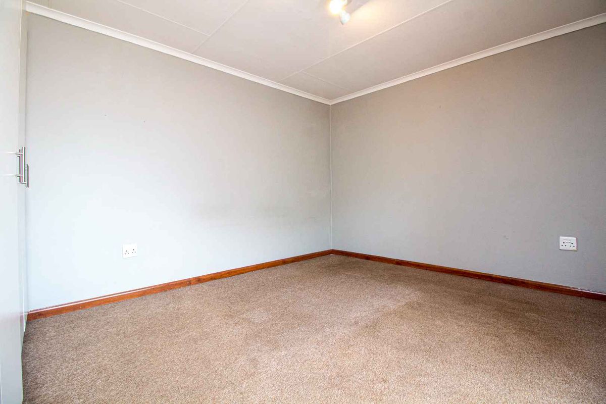 A vacant bedroom featuring neutral grey walls, brown carpeting, and a built-in cupboard with white doors.