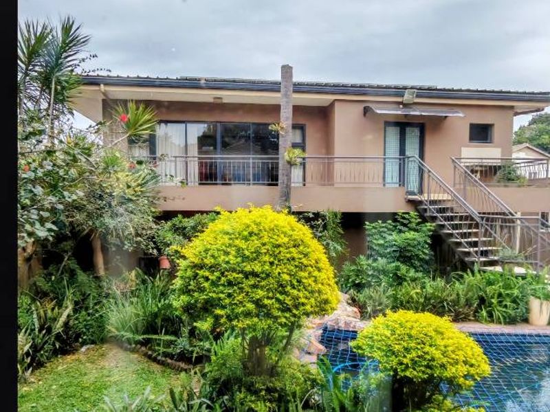 Rear view of the house featuring a swimming pool, landscaped garden, paved patio area, and an elevated balcony with metal railings.
