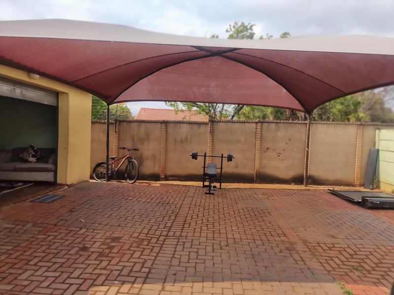 A covered outdoor patio area featuring paved flooring and a large shade sail, providing a functional space for outdoor activities.