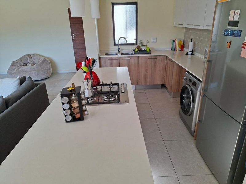 Open-plan kitchen featuring a central island with a gas hob, modern cabinetry, tiled flooring, and integrated laundry appliances.
