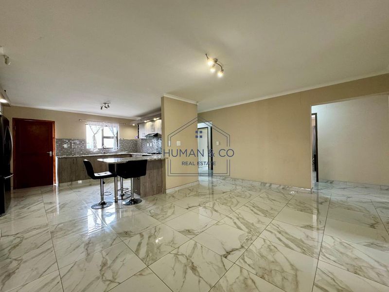 Open-plan living area featuring marble-look floor tiles and a modern kitchen with granite countertops, built-in cabinetry, and integrated appliances.