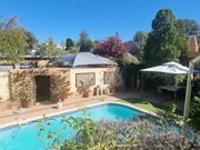 Outdoor pool area featuring a swimming pool, paved patio space, and surrounding boundary walls in a landscaped garden setting.