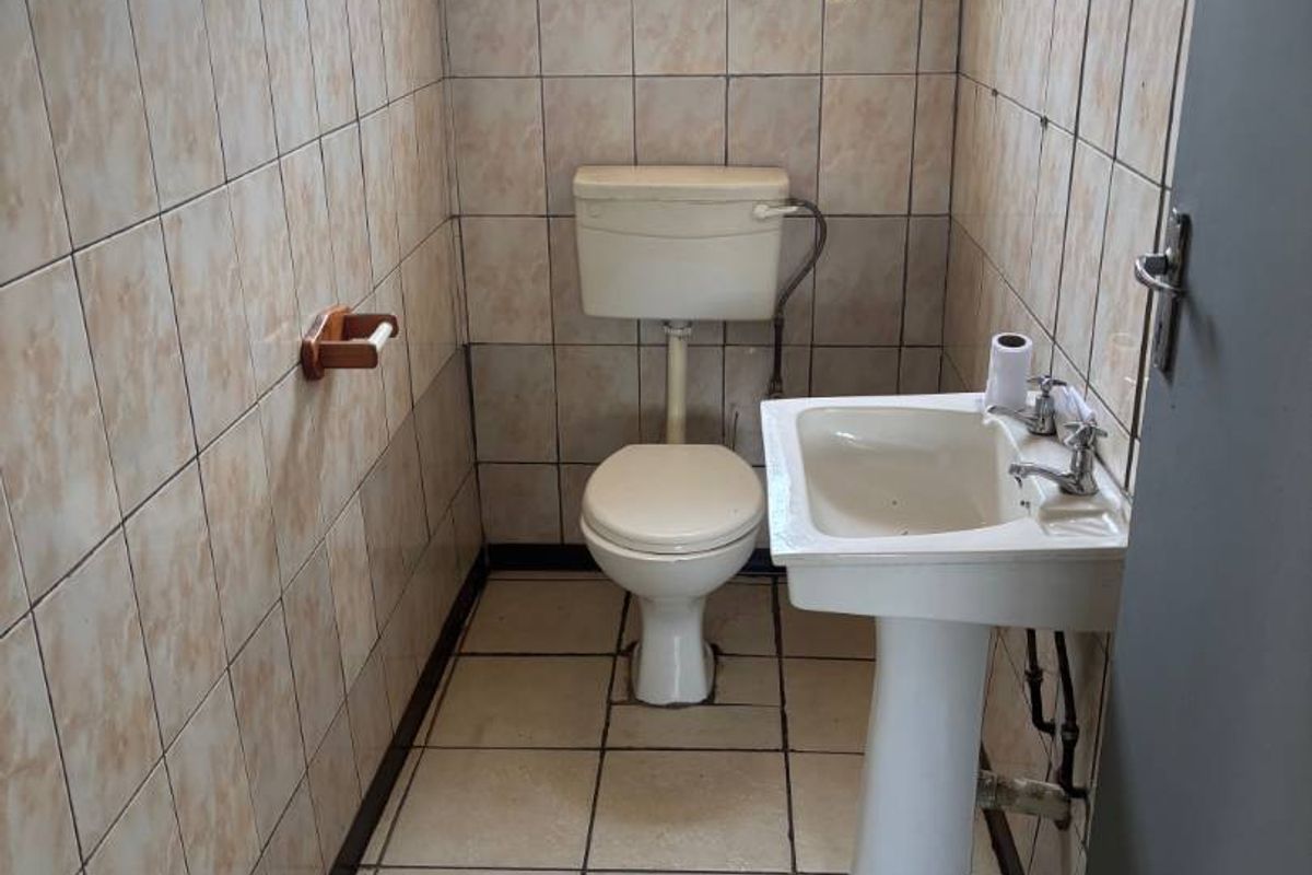 A compact guest bathroom featuring a pedestal basin, toilet, and full-height ceramic wall tiling, currently in need of cosmetic updates.