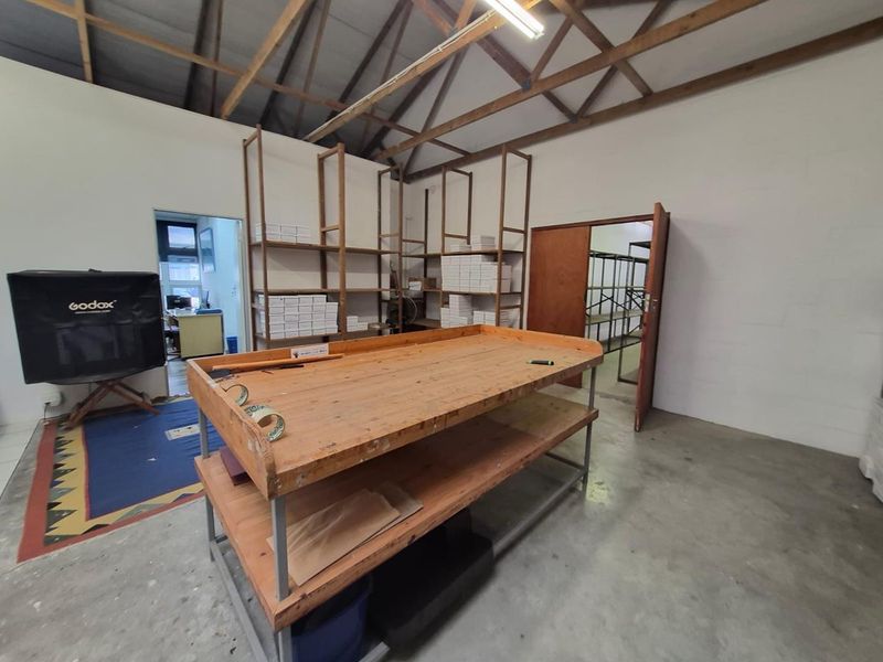 A functional utility or storage space featuring exposed timber roof trusses, concrete flooring, and built-in shelving units.