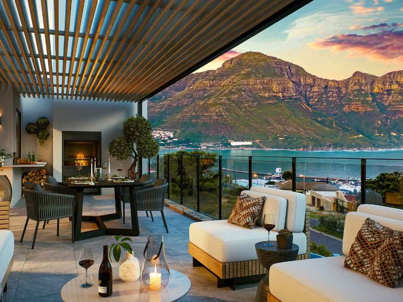 Spacious covered balcony featuring a built-in fireplace, slatted pergola, and glass balustrade, offering stunning panoramic mountain and coastal views.