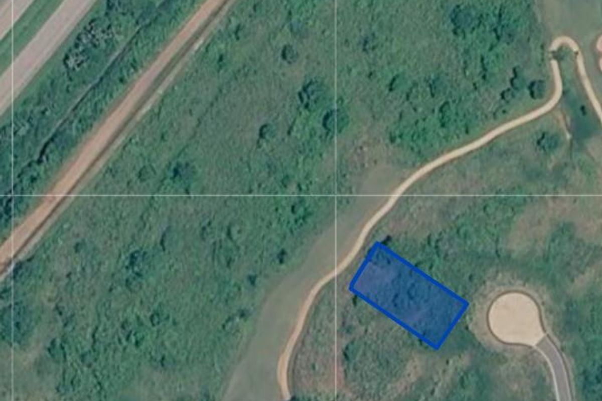 Aerial view of a vacant residential plot of land with surrounding natural vegetation and access road infrastructure.