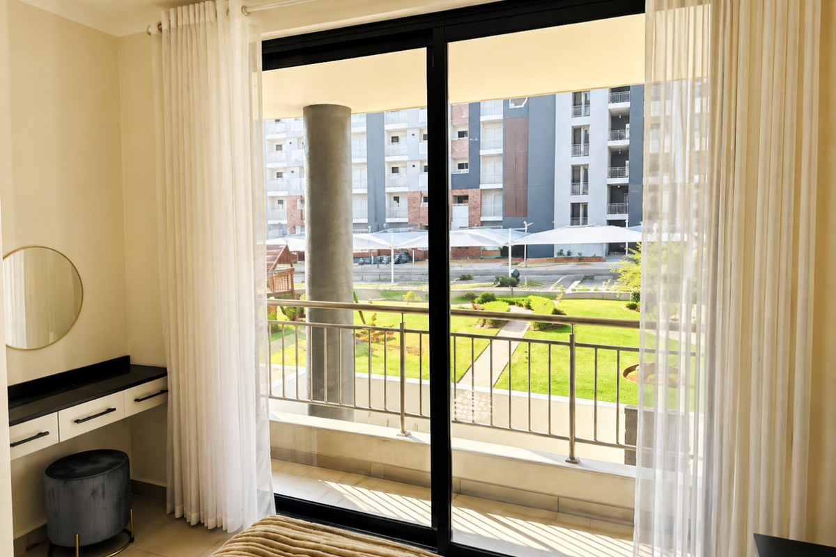 A bright bedroom featuring a built-in vanity and a large sliding glass door that opens onto a private balcony with garden views.